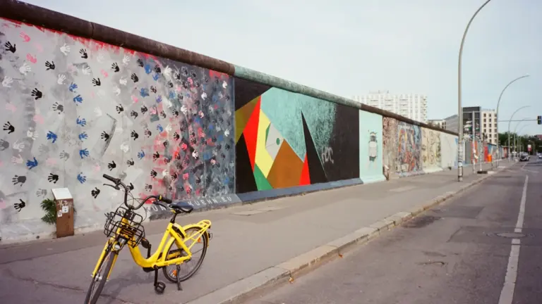 Ein gelbes Fahrrad steht vor einem mit Graffitis bemalten Abschnitt der Berliner Mauer.