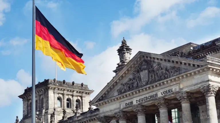 Die deutsche Flagge weht vor dem historischen Reichstagsgebäude unter blauem Himmel in Berlin.