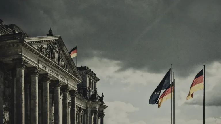 Der deutsche Reichstag unter einem wolkenverhangenen Himmel mit wehenden Flaggen in Berlin.
