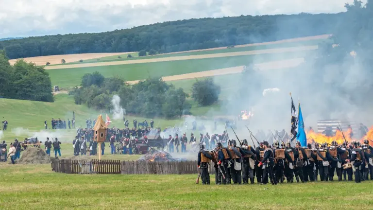Historische Nachstellung einer Schlacht mit Soldaten, Pulverdampf und brennendem Dorf auf dem Feld.