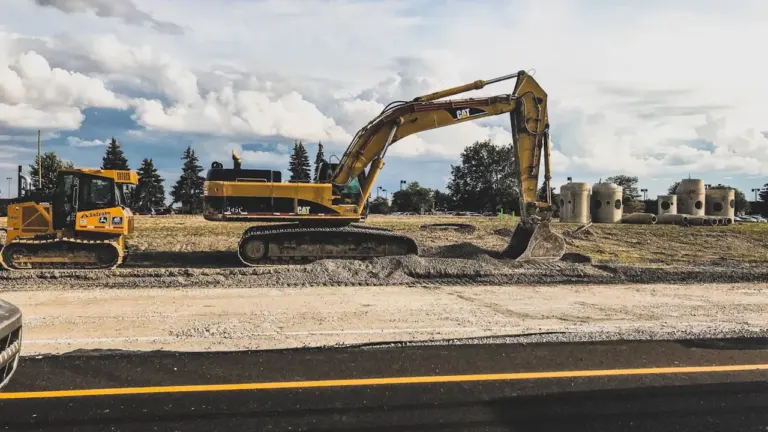 Gelber Bagger bei Bauarbeiten an einer Straße unter bewölktem Himmel