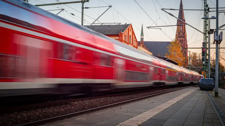 Ein roter Regionalzug fährt in einem deutschen Bahnhof am Gleis entlang vorbei.