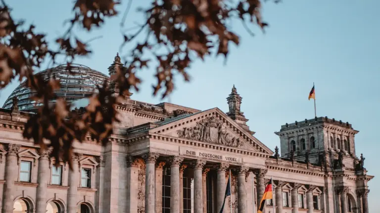Das Reichstagsgebäude in Berlin unter blauem Himmel mit der wehenden Deutschlandfahne.