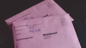 Rosa Wahlbrief-Umschläge für die Briefwahl liegen bereit auf einem dunklen Tisch.