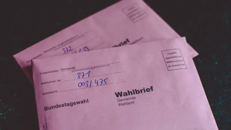 Rosa Wahlbrief-Umschläge für die Briefwahl liegen bereit auf einem dunklen Tisch.
