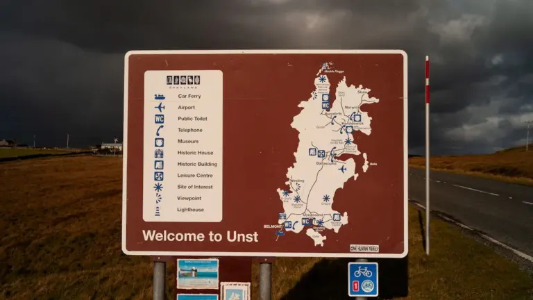 Ein Hinweisschild mit einer Umgebungskarte am Straßenrand unter einem bewölkten, stürmischen Himmel.