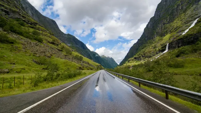 Nasse Landstraße durch eine norwegische Berglandschaft bei bewölktem und stürmischem Wetter.