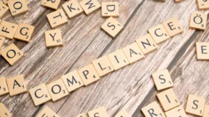 Holzbuchstaben bilden das Wort Compliance auf einem hölzernen Schreibtischhintergrund für rechtliche Themen.