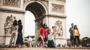 Familie macht ein Selfie vor dem Triumphbogen in Paris bei sonnigem Tageslicht.