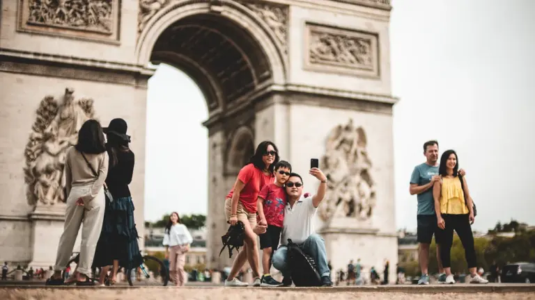 Familie macht ein Selfie vor dem Triumphbogen in Paris bei sonnigem Tageslicht.