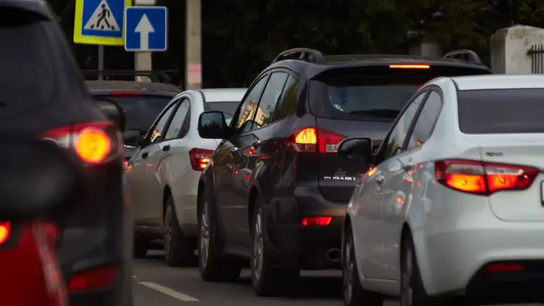 Dichte Autoschlange im Stadtverkehr vor einer Kreuzung mit Straßenschildern bei Tageslicht.