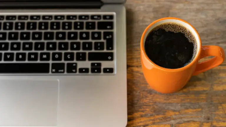 Ein Laptop steht auf einem Holztisch neben einer Tasse mit schwarzem Kaffee.