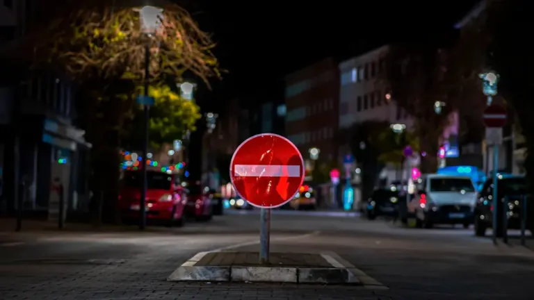 Ein beleuchtetes Durchfahrtsverbotsschild steht bei Nacht auf einer leeren innerstädtischen Straße.