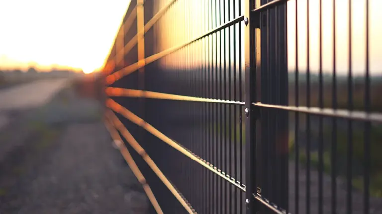Ein schwarzer Metallzaun vor einem Sonnenuntergang, der die Grenze zwischen Freiheit und Isolation symbolisiert.
