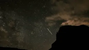Ein Sternschnuppenschauer am nächtlichen Sternenhimmel über einer dunklen Gebirgssilhouette bei Nacht.