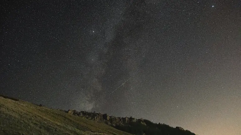 Sternenhimmel über einem sanften grasbewachsenen Hügel in einer klaren Sommernacht in Deutschland.