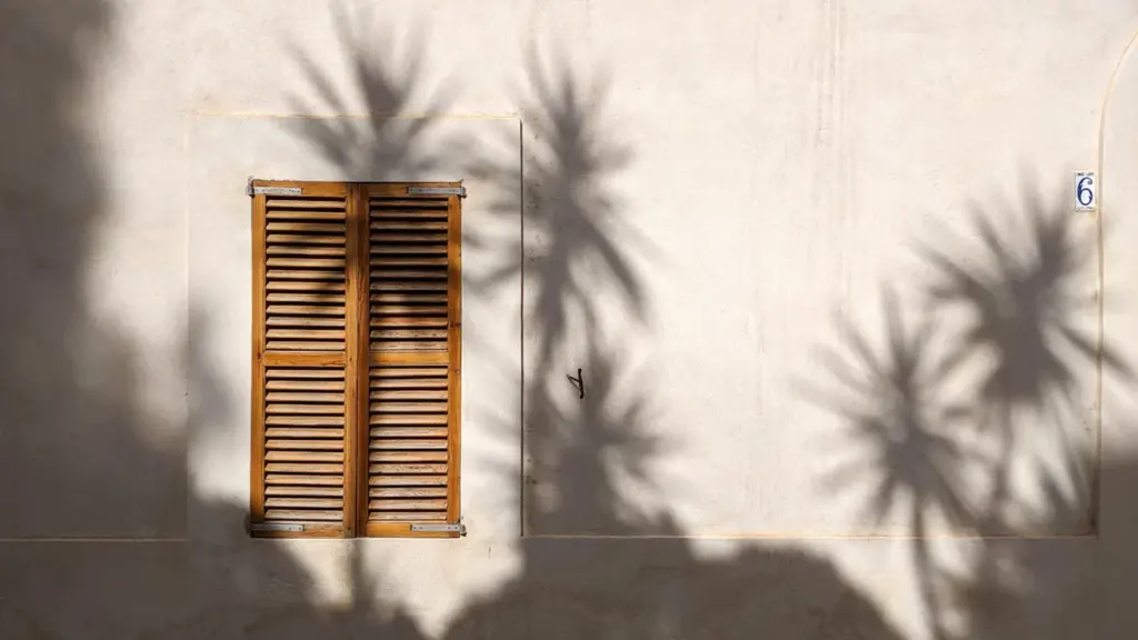 Geschlossene Fensterläden an einer Hausfassade bei sonnigem Wetter zur Hitzeprävention.