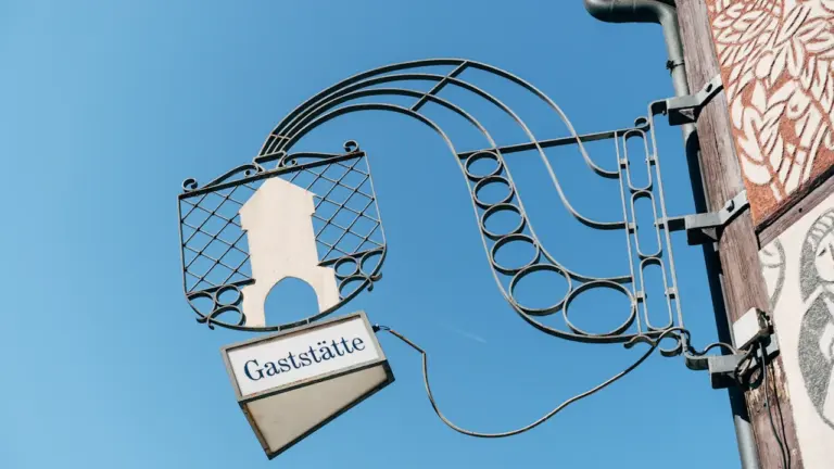 Traditionelles schmiedeeisernes Gaststättenschild an einem historischen Fachwerkhaus in einer deutschen Stadt.