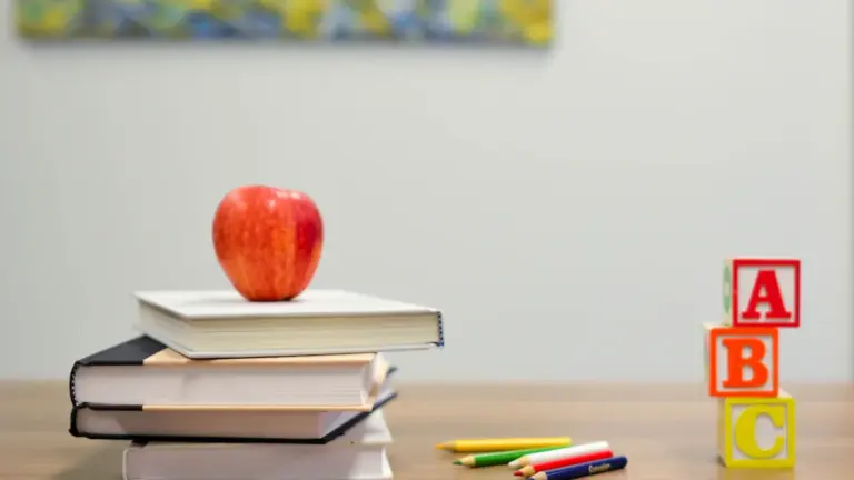 Bücherstapel mit rotem Apfel und ABC-Bausteinen auf einem Schreibtisch.