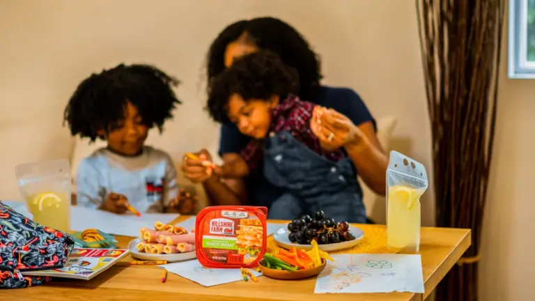 Familie beim Vorbereiten und gemeinsamen Essen am Tisch vor dem Schulstart.