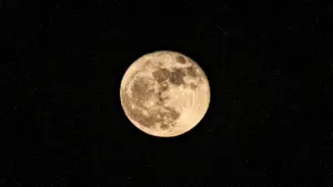 Ein heller Vollmond leuchtet detailliert vor einem tiefschwarzen, sternenreichen Nachthimmel in der Dunkelheit.