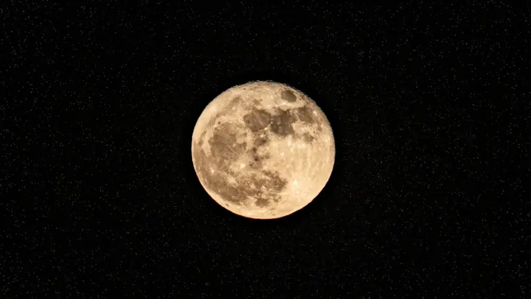 Ein heller Vollmond leuchtet detailliert vor einem tiefschwarzen, sternenreichen Nachthimmel in der Dunkelheit.