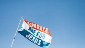 Eine wehende Flagge mit der Aufschrift 'Sundays are for Jesus' vor blauem Himmel.