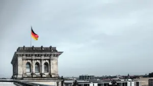 Blick auf das Berliner Reichstagsgebäude mit wehender Deutschlandflagge unter bewölktem Himmel.