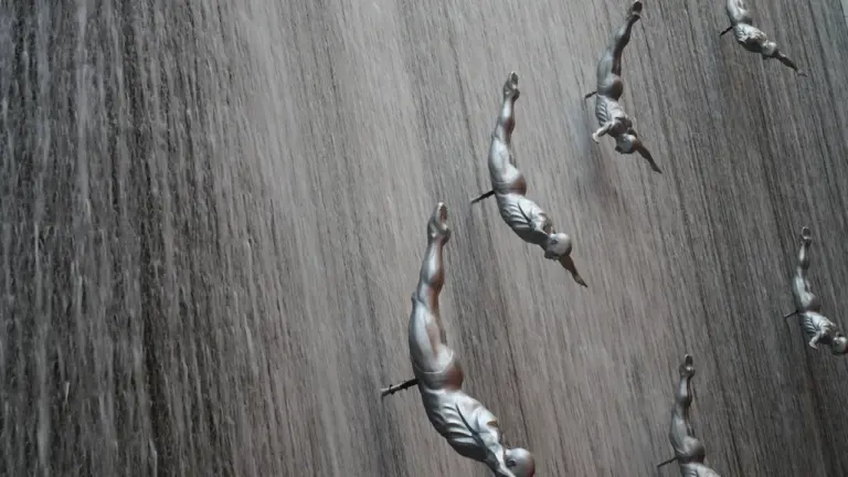 Abstrakte Skulpturen von fallenden Menschen an einer grauen Wand