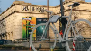 Ein weißes Fahrrad steht vor dem Münchner Haus der Kunst mit einer Ausstellungstafel.