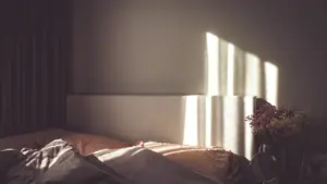 Sanftes Morgenlicht fällt durch ein Fenster in ein gemütliches, ungemachtes Schlafzimmer.